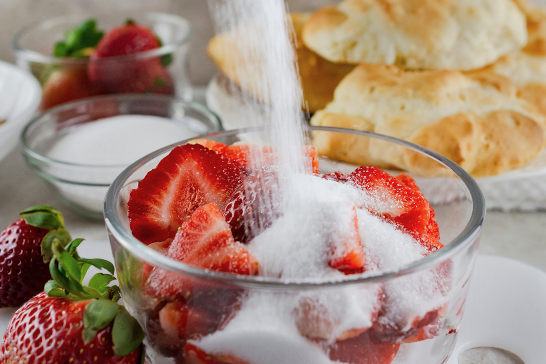 Gros plan sur l'ajout de sucre dans un saladier de fraises coupées en tranches