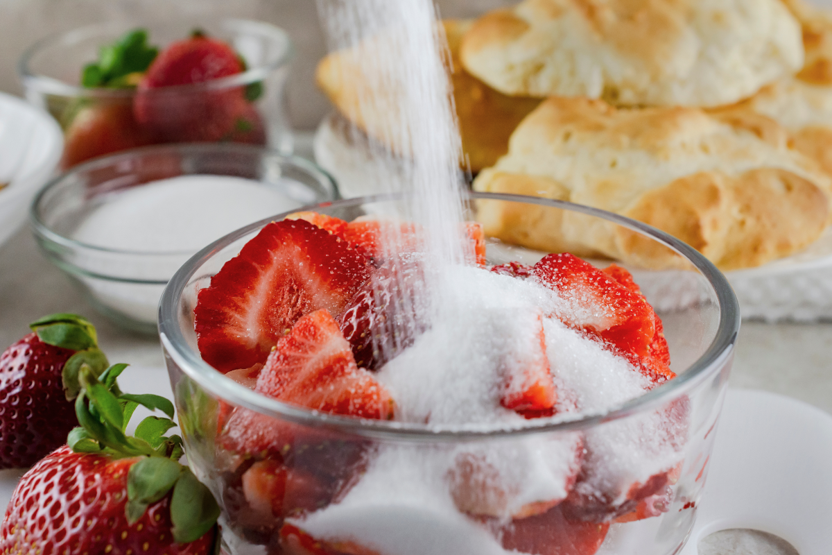 Gros plan sur l'ajout de sucre dans un saladier de fraises coupées en tranches